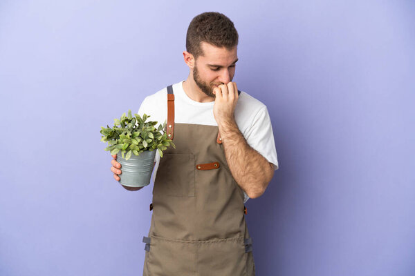 Gardener caucasian man holding a plant isolated on yellow background having doubts