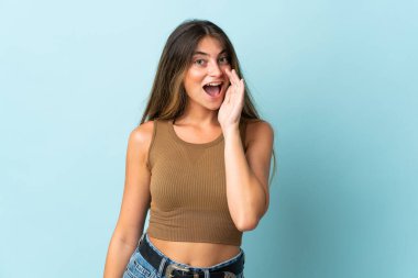 Mavi arka planda izole edilmiş genç beyaz kadın ağzı açık bağırıyor.