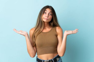 Mavi arka planda izole edilmiş genç beyaz kadın şüpheli hareketler yapıyor.