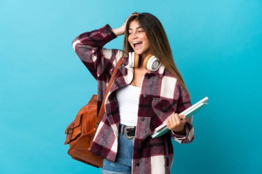 Genç bayan öğrenci, mavi arka planda izole edilmiş, çok gülümsüyor.