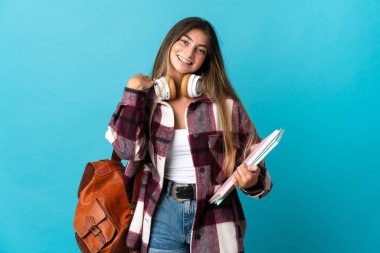 Genç bir bayan öğrenci mavi arka planda yalnız gülüyor.