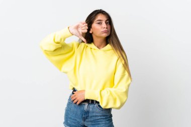 Beyaz arka planda izole edilmiş genç beyaz kadın olumsuz ifade ile baş parmağını aşağı gösteriyor.