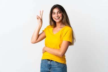 Beyaz arka planda izole edilmiş genç beyaz kadın gülümsüyor ve zafer işareti gösteriyor.