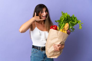 Market poşeti tutan genç bir kadın telefon jesti yapıyor. Bana geri dönüş işareti ver.