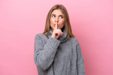 Pembe fırında izole edilmiş genç beyaz kadın parmağını ağzına koyduğunda sessizlik işareti gösteriyor.