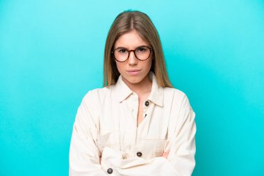 Mavi arka planda izole edilmiş, kolları ve gözlükleri çaprazlanmış beyaz bir kadın.