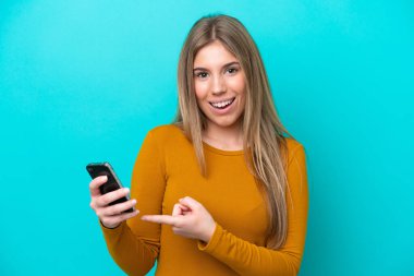 Genç beyaz kadın mavi arka planda izole edilmiş ve cep telefonu kullanıyor.