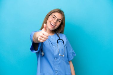 Genç cerrah kadın doktor mavi arka planda izole edildi. Başparmakları havada çünkü iyi bir şey oldu.