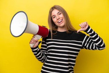 Sarı arka planda izole edilmiş genç beyaz kadın elinde megafonla gururlu ve kendini beğenmiş.