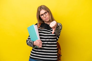 Sarı arka planda izole edilmiş genç bir bayan, olumsuz ifade ile baş parmağını gösteriyor.