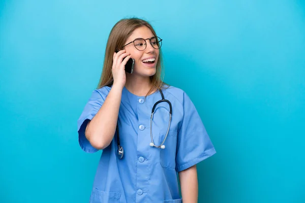一位年轻的外科医生 她被隔离在蓝色背景下 与手机保持对话 — 图库照片