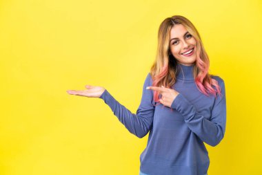 İzole edilmiş sarı arka plan üzerinde genç bir kadın. Avucunun içinde bir reklam koymak için hayali bir alan tutuyor.