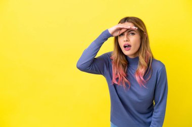 Izole sarı arka plan üzerinde genç kadın uzak el ile bir şey bakmak için bakıyor