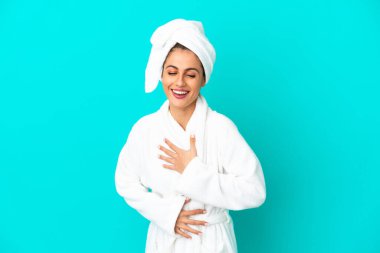 İzole edilmiş mavi arka planı olan bornozlu genç bir kadın çok gülümsüyor.