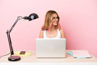 İş yerinde pembe arka planda dizüstü bilgisayarı olan genç bir bayan öğrenci.