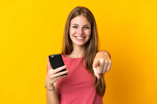Молода Жінка Використовує Мобільний Телефон Ізольовано Жовтому Фоні Вказує Пальцем — стокове фото
