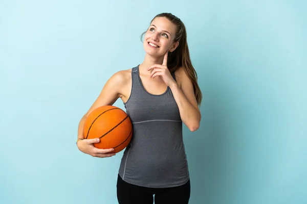 青い背景に孤立したバスケットボールをしている若い女性がアイデアを考えながら検索 — ストック写真