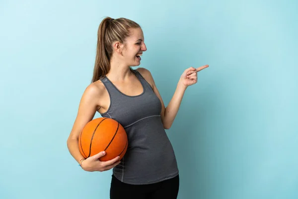 파란색 배경에서 고립된 농구를 손가락으로 가리키며 제품을 제공하는 — 스톡 사진