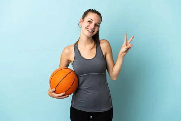 若いです女性プレーバスケットボール孤立した上に青の背景笑顔と勝利サインを示す — ストック写真