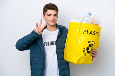 Beyaz arka planda geri dönüşüm yapmak için elinde plastik şişelerle dolu bir çanta tutan genç Rus mutlu ve parmaklarıyla üçe kadar sayıyor.