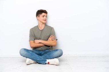 Genç Rus adam beyaz arka planda, kolları bağlı ve mutlu bir şekilde yerde oturuyor.