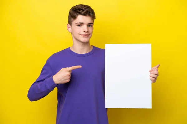 十代のロシア人の男は幸せな表情で空のプラカードを保持し それを指す黄色の背景に隔離 — ストック写真