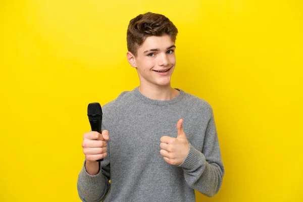 Співак Підліток Збирає Мікрофон Ізольований Жовтому Тлі Великими Пальцями Тому — стокове фото
