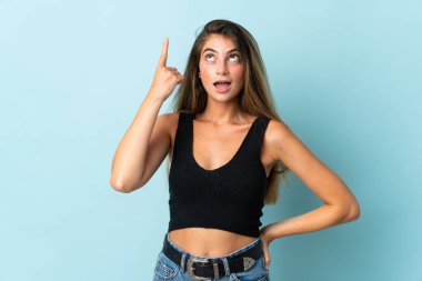 Kafkasyalı genç kadın mavi arka planda izole edildi. Çözümün farkına varmak için parmağını kaldırdı.