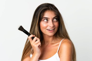 Beyaz arka planda izole edilmiş beyaz bir kadın elinde makyaj fırçası ve yukarı bakıyor.