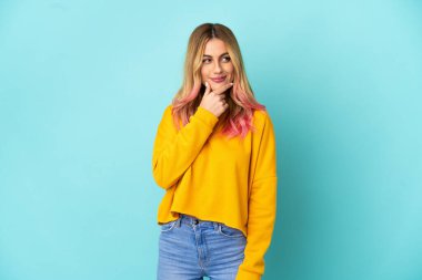 Soyutlanmış mavi arka planda genç bir kadın yana bakıyor ve gülümsüyor.