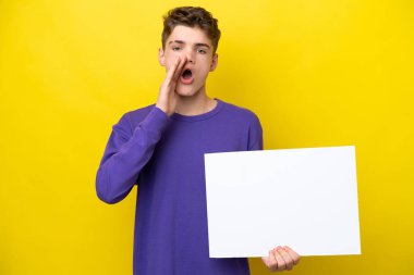 Genç Rus adam sarı arka planda izole edilmiş. Elinde boş bir levha var ve bağırıyor.
