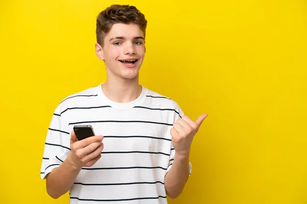 Teenager Russian Man Isolated Yellow Background Using Mobile Phone Pointing — Stock Photo, Image