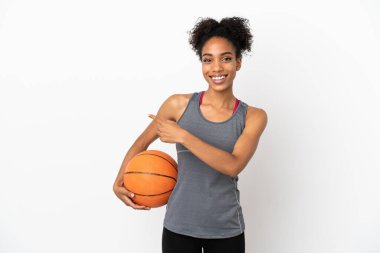 Genç basketbolcu Latin kadın, beyaz arka planda izole edilmiş basketbol oynuyor ve yan tarafı işaret ediyor.
