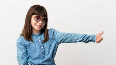 Güneş gözlüklü küçük kız beyaz arka planda izole edilmiş bir şekilde baş parmak hareketi yapıyor.