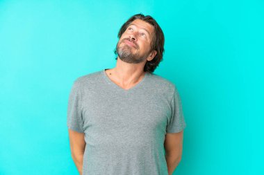 Kıdemli Hollandalı adam mavi arka planda izole edilmiş ve araştırılıyor.