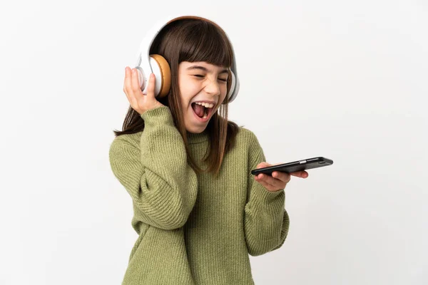 小さな女の子リスニング音楽とともにモバイル隔離されたオンホワイトバックグランドリスニング音楽とともにモバイルと歌 — ストック写真