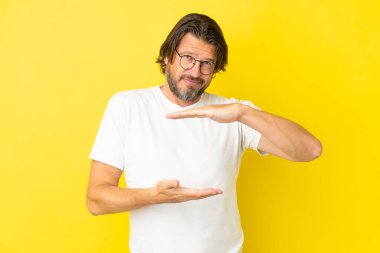 Kıdemli Hollandalı, sarı arka planda izole edilmiş. Elinde bir ilan vermek için avucunda hayali bir alan tutuyor.