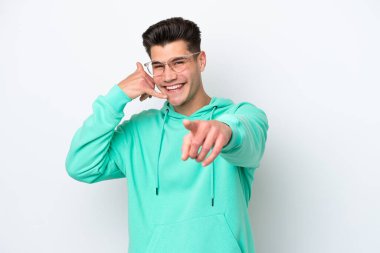 Beyaz fırında izole edilmiş genç, yakışıklı beyaz bir adam telefon hareketi yapıyor ve ön tarafı işaret ediyor.