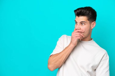 Genç, yakışıklı, beyaz bir adam, mavi bakkalda izole edilmiş. Yan tarafa bakarken sürpriz jest yapıyor.