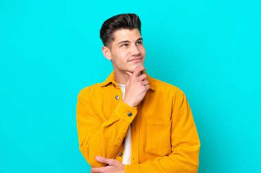 Genç, yakışıklı, beyaz bir adam, mavi bir fırında izole edilmiş bir şekilde yukarı bakarken bir fikir düşünüyor.