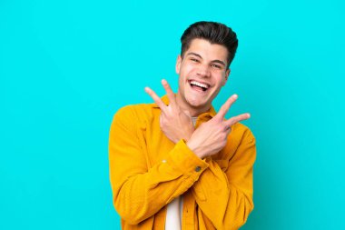 Genç, yakışıklı, beyaz bir adam mavi bir bakkalda izole edilmiş gülümsüyor ve zafer işareti gösteriyor.