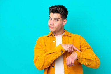 Genç, yakışıklı, beyaz bir adam, mavi bakkalda izole edilmiş, geç kalma jesti yapıyor.