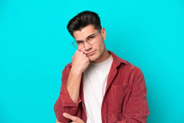 Genç, yakışıklı, beyaz bir adam mavi fırında tek başına, gözlüklü ve üzgün bir ifadeyle.