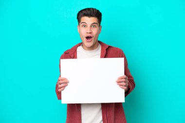 Genç, yakışıklı, beyaz bir adam mavi bir bakkalda izole edilmiş, elinde mutlu bir ifadeyle boş bir levha tutuyor.