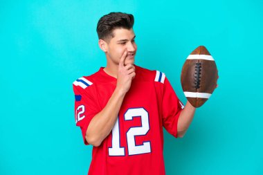 Rugby oynayan genç beyaz adam mavi arka planda izole edilmiş bir şekilde yukarı bakarken bir fikir düşünüyor.