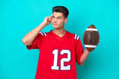 Rugby oynayan beyaz bir adam mavi arka planda izole edilmiş. Şüpheleri ve düşünceleri var.