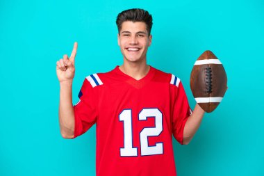 Genç beyaz adam rugby oynuyor. Mavi arka planda izole edilmiş. Harika bir fikre işaret ediyor.