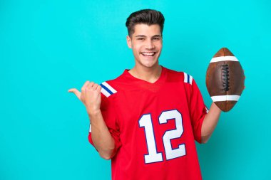 Rugby oynayan beyaz bir genç, mavi arka planda izole edilmiş bir şekilde bir ürünü sunmak için yan tarafa bakıyor.