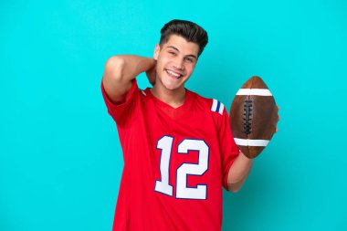 Rugby oynayan Kafkasyalı genç adam mavi arka planda izole bir şekilde gülüyor.