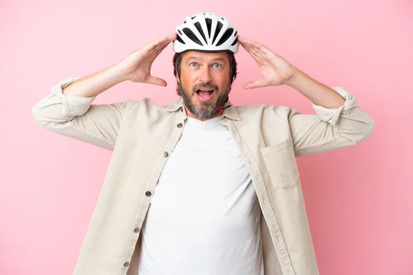 驚きの表情でピンクの背景に隔離された自転車のヘルメットを持つシニアオランダ人男性 — ストック写真
